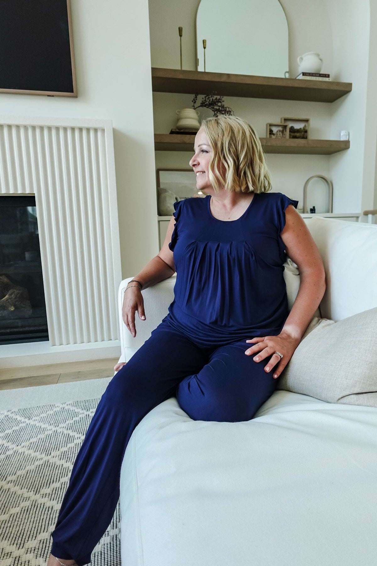 woman sitting on white couch in dark navy blue pajama set with flattering top and jogger pant with drawstring and pockets