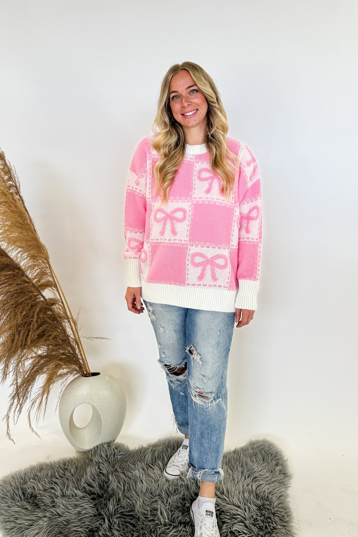 woman standing wearing a pink and white sweater with pink bow details 