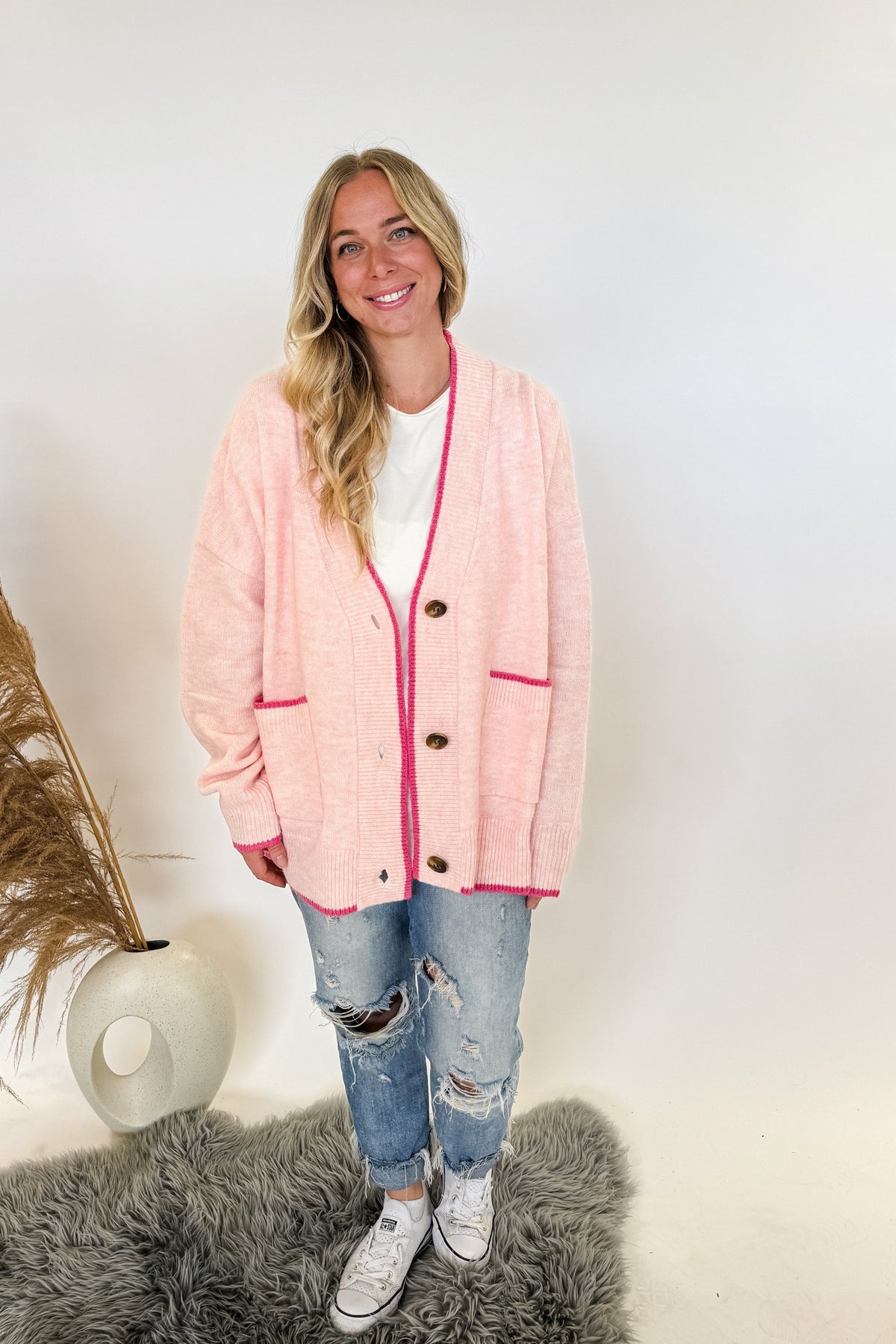 woman stands wearing an oversized cardigan in light pink with bows on the elbows and hot pink trim