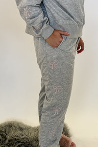 woman standing wearing a grey sweat suit with pink bow details and fuzzy pink slippers