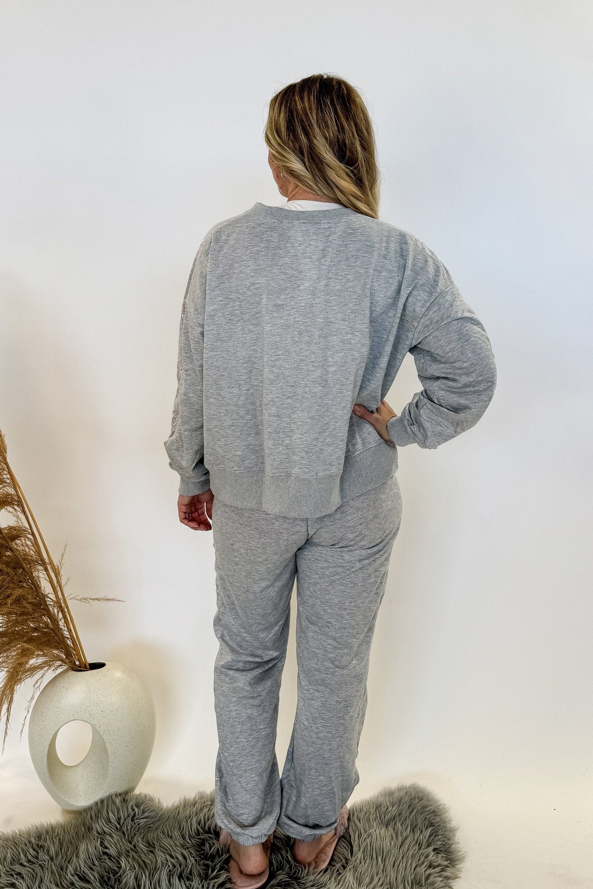 woman standing wearing a grey sweat suit with pink bow details and fuzzy pink slippers