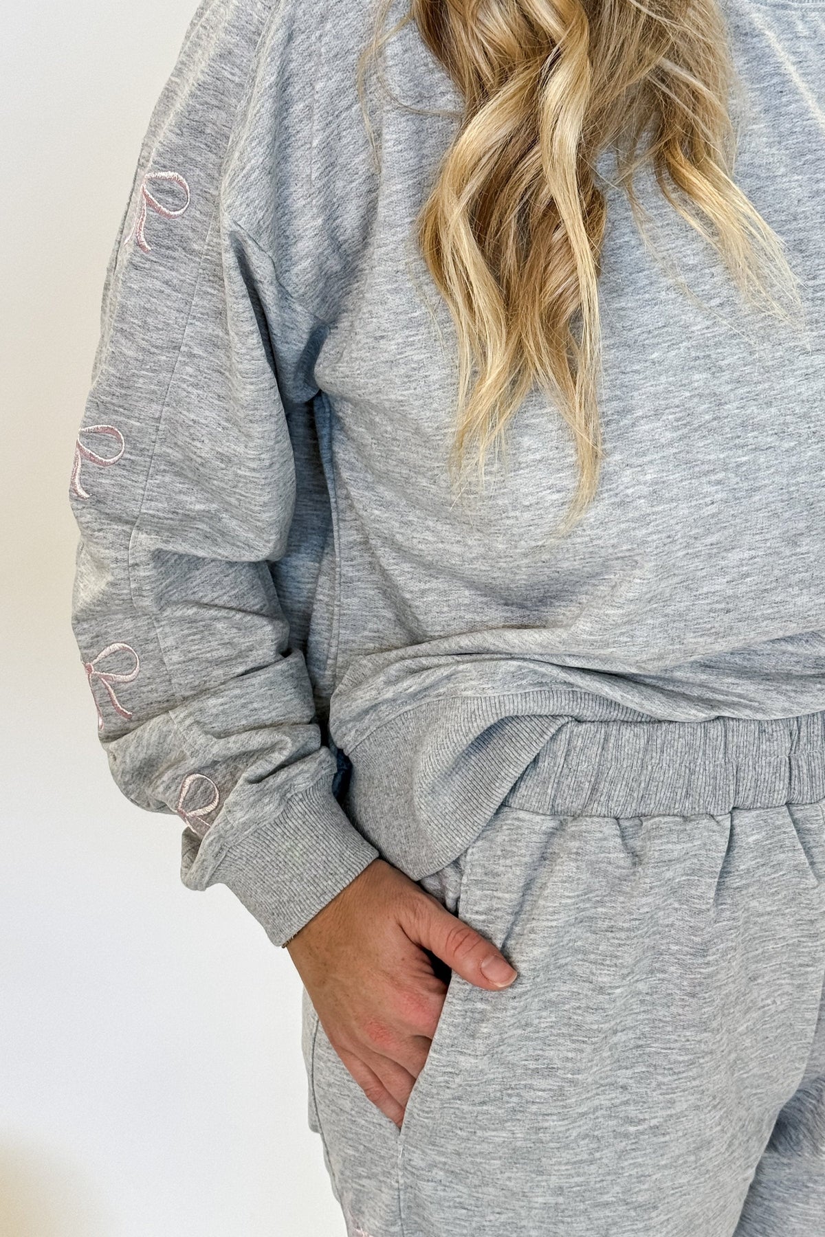 woman standing wearing a grey sweat suit with pink bow details and fuzzy pink slippers